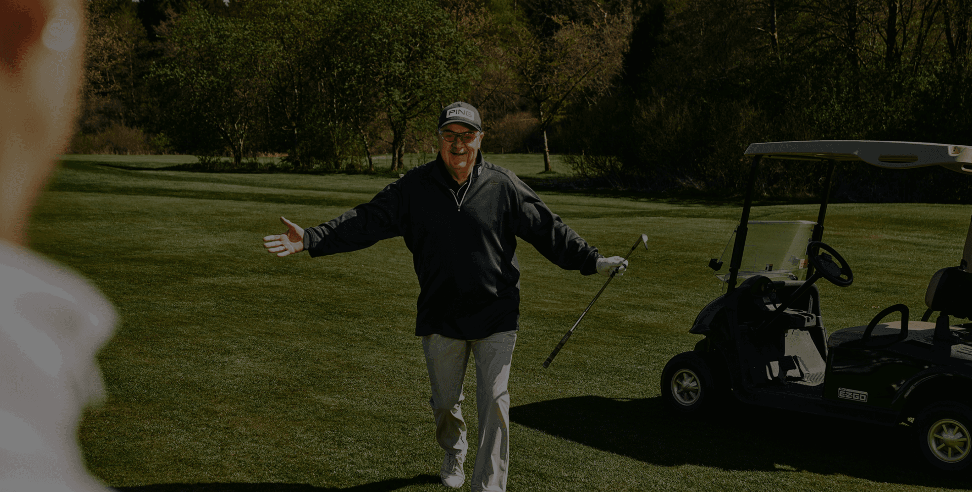 Golfer begrüßt freudig neben Golfwagen auf grünem Fairway.