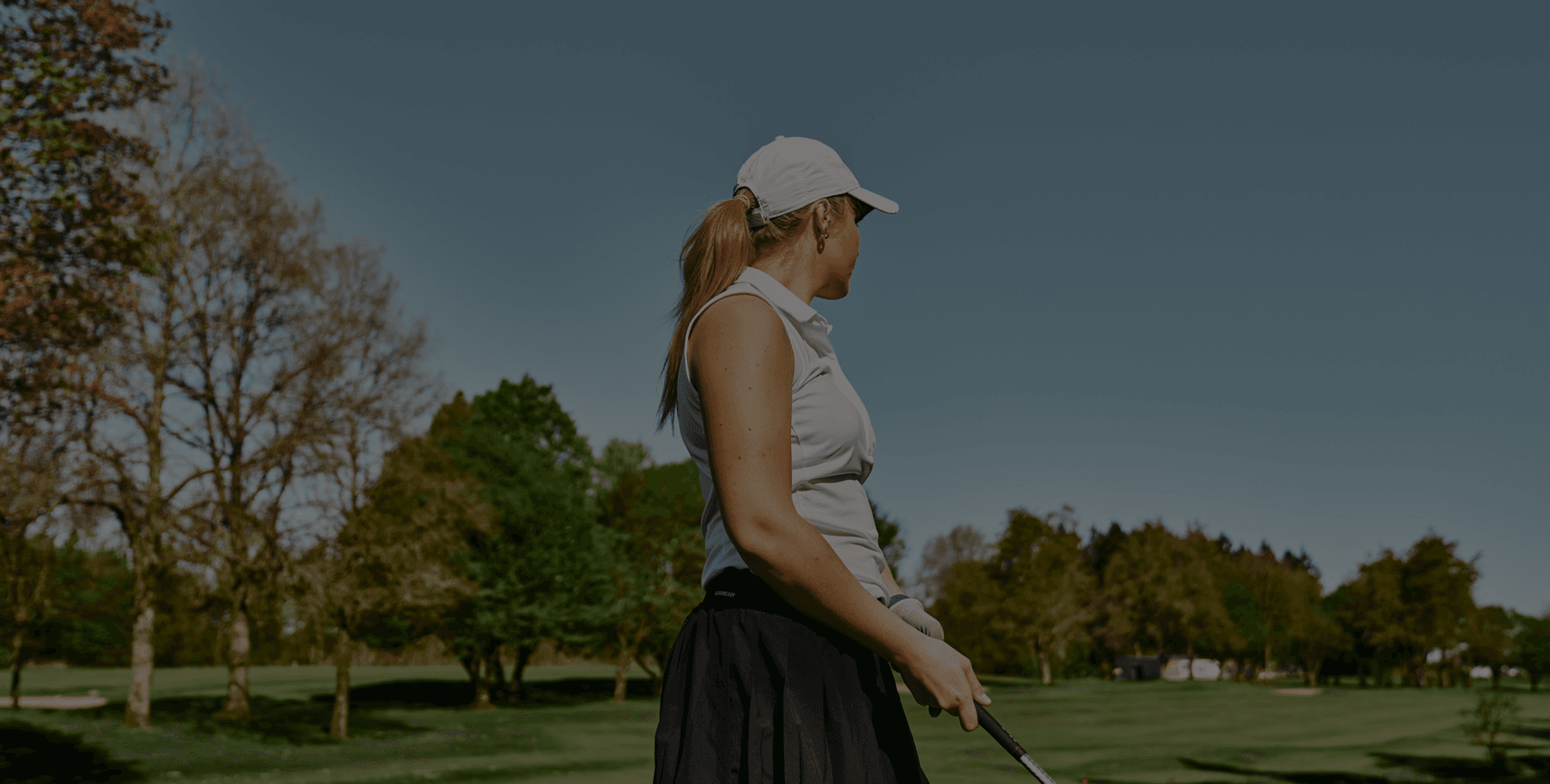Golferin auf sonnigem Platz, umgeben von Bäumen im Frühling