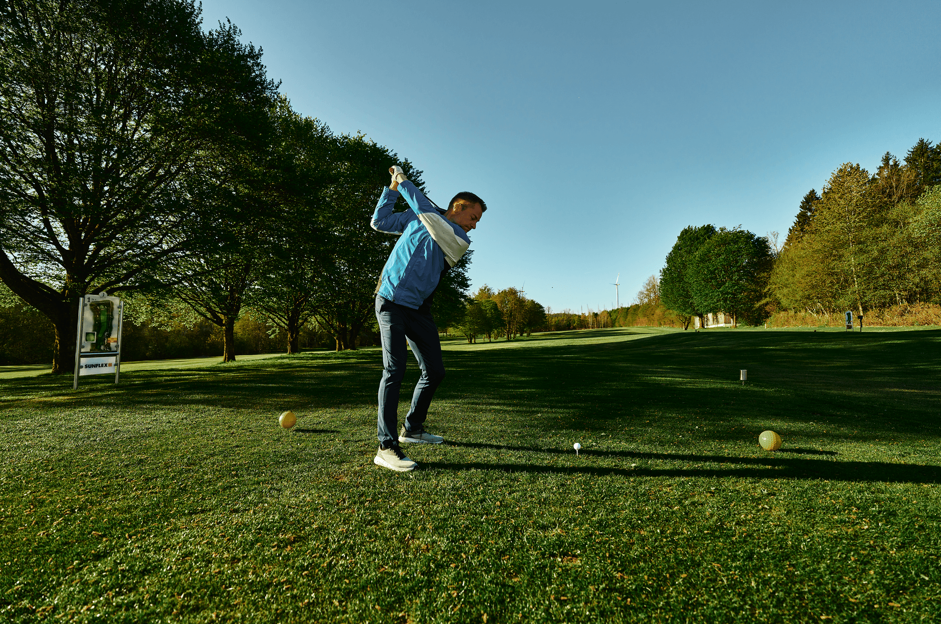 Golfer beim Abschlag auf grünem Fairway unter blauem Himmel