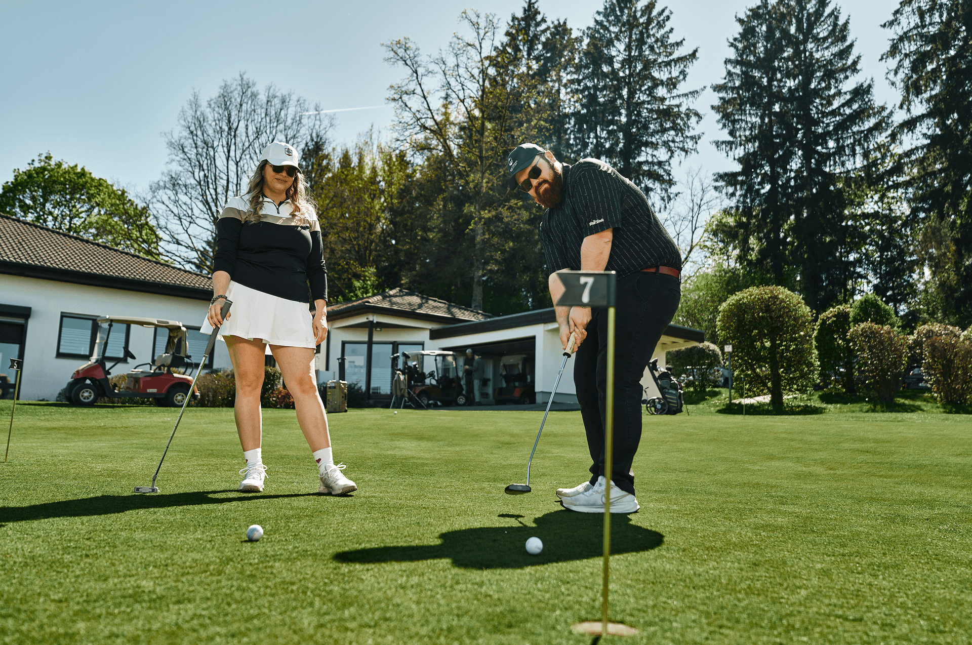 Zwei Golfer beim Putten auf einem grünen Platz im Sonnenschein
