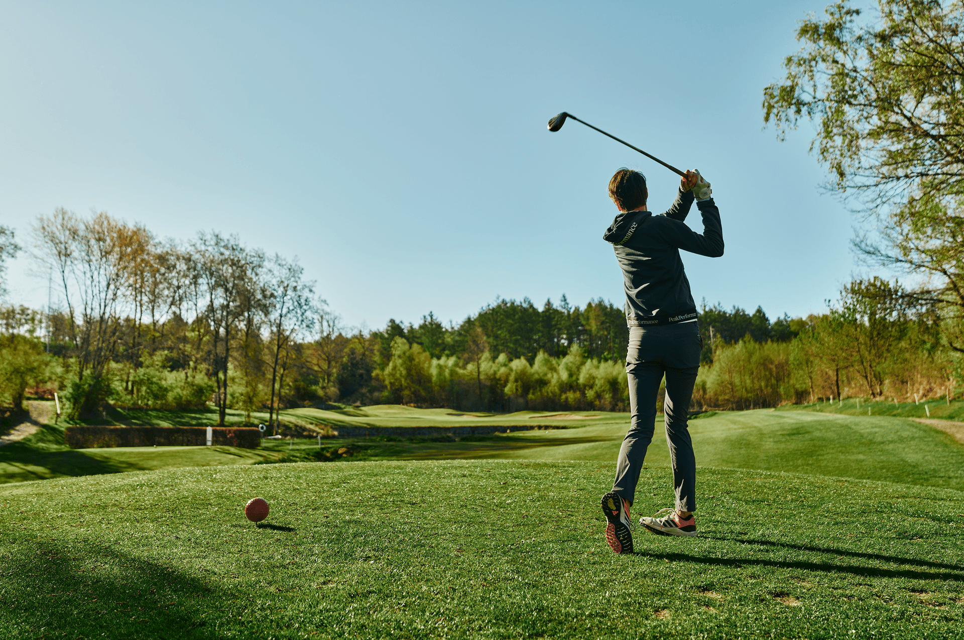 Golfspieler beim Abschlag auf gepflegtem Grün vor malerischer Waldkulisse