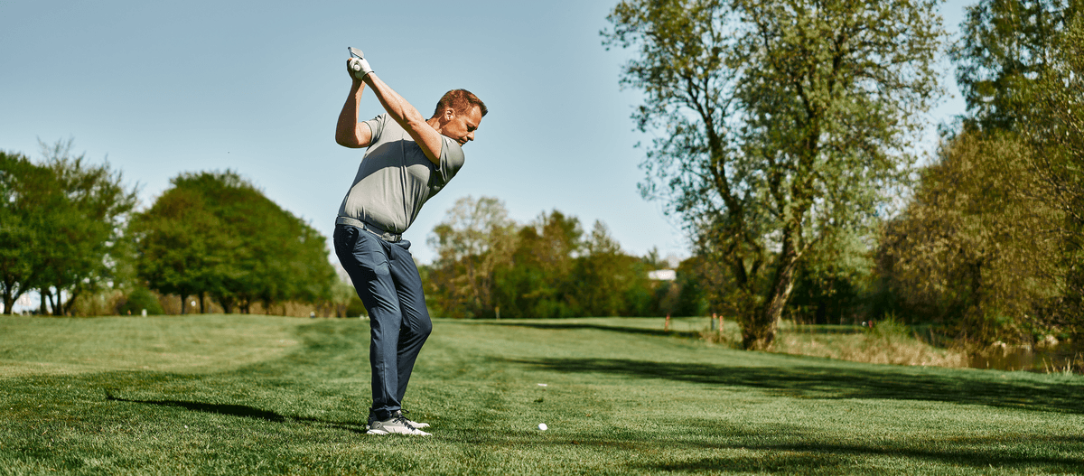 Golfer beim Abschlag auf einer grünen Fairway im Sonnenschein