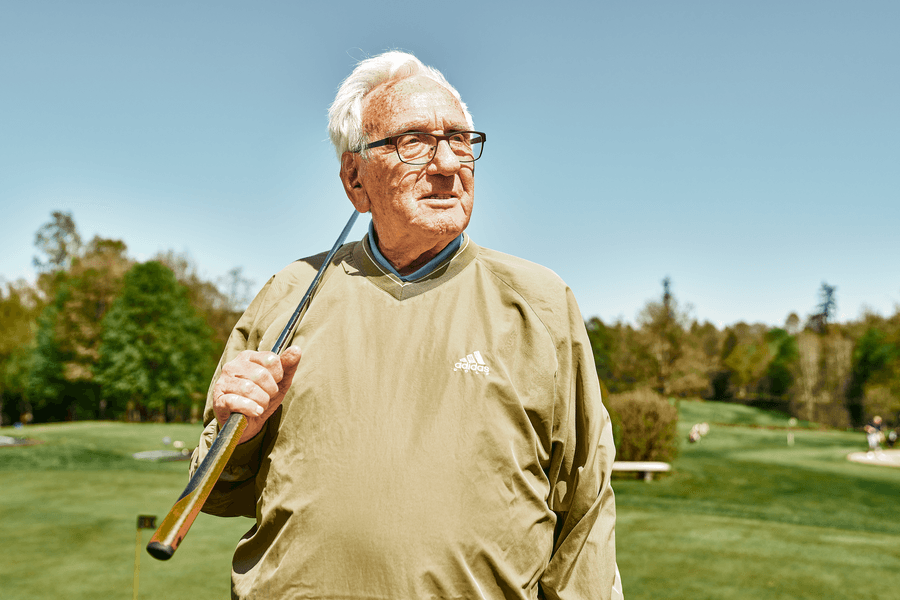 Älterer Mann mit Golfschläger auf dem Golfplatz, umgeben von grüner Landschaft