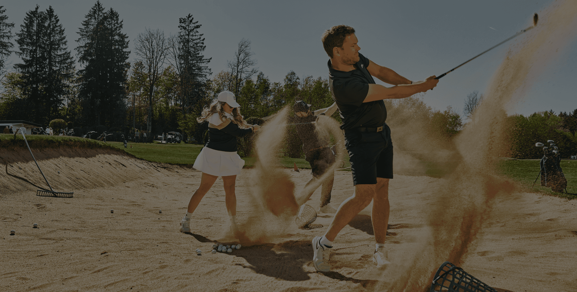 Golfer trainieren Schwünge im Sandbunker auf einem sonnigen Golfplatz.