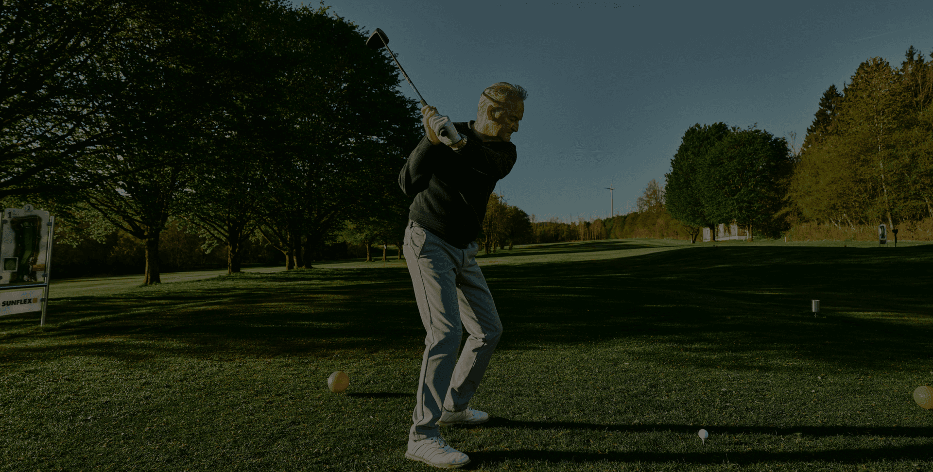 Golfer beim Abschlag auf grünem Fairway im Morgenlicht