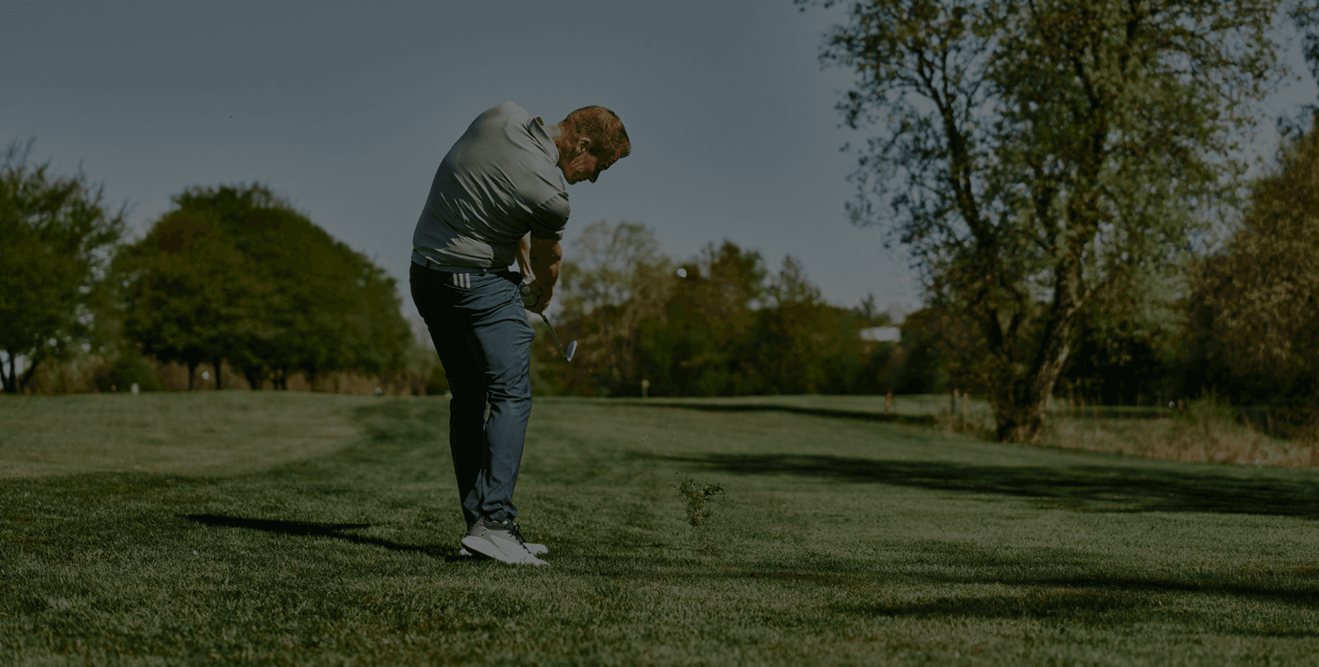 Golfer beim Abschlag auf gepflegtem Fairway, umgeben von Bäumen und Natur.