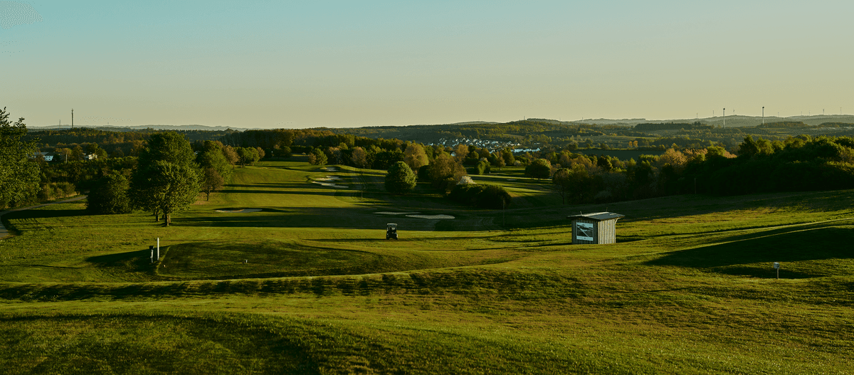 Weitläufige Golfplatzlandschaft im Abendlicht mit Blick auf sanfte Hügel.
