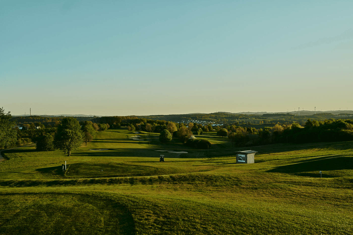 Weitläufige Golfplatzlandschaft im Abendlicht mit Blick auf sanfte Hügel.