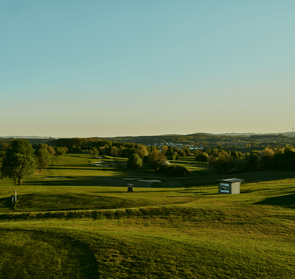 Weitläufige Golfplatzlandschaft im Abendlicht mit Blick auf sanfte Hügel.