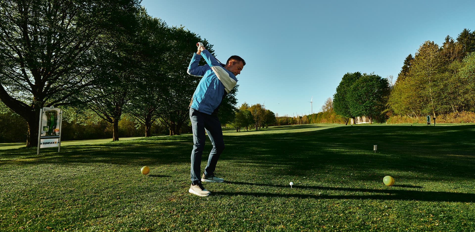 Golfer beim Abschlag auf grüner Anlage bei bestem Wetter