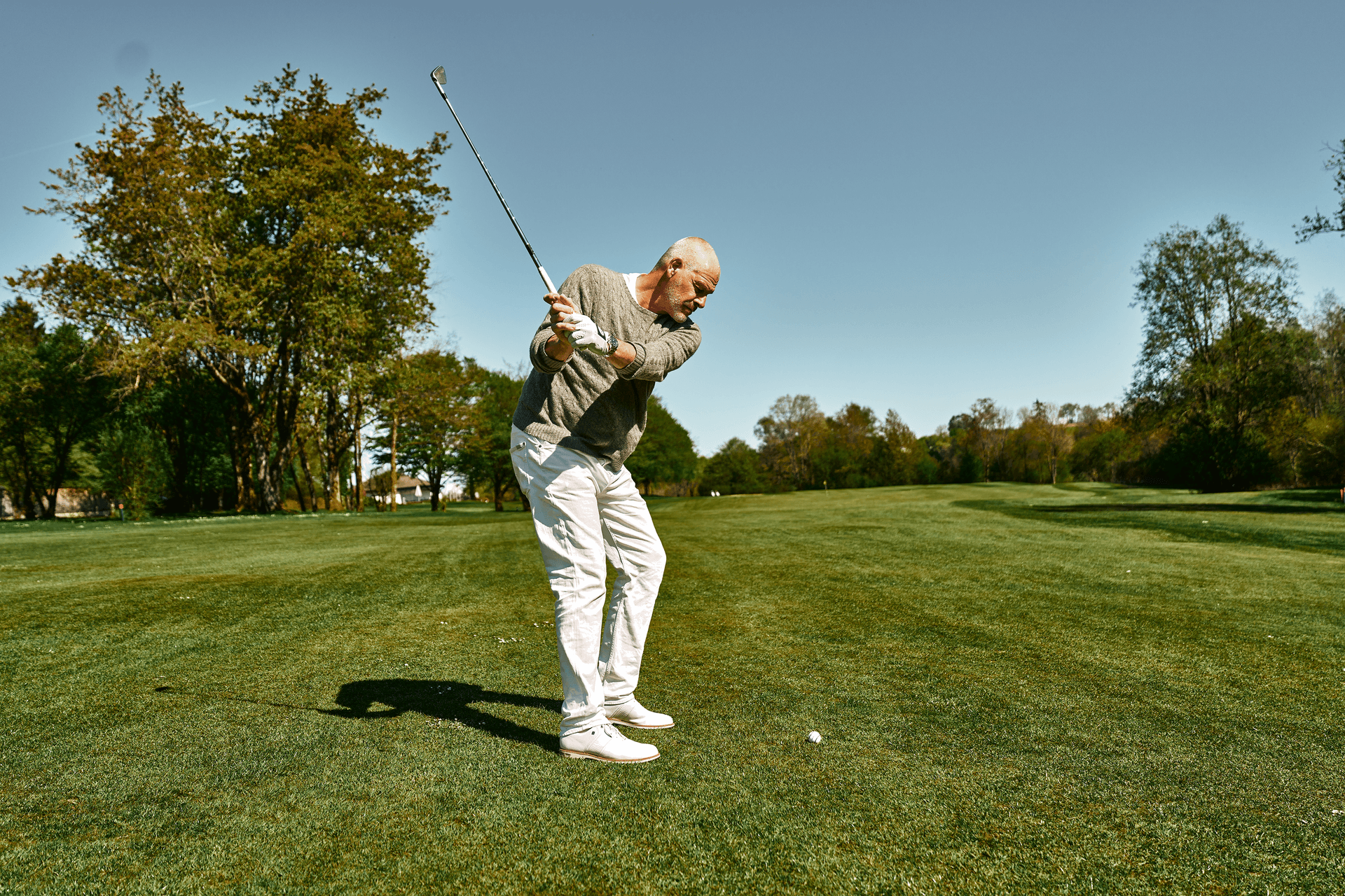 Golfer beim Abschlag auf einem grünen Fairway im Sonnenschein