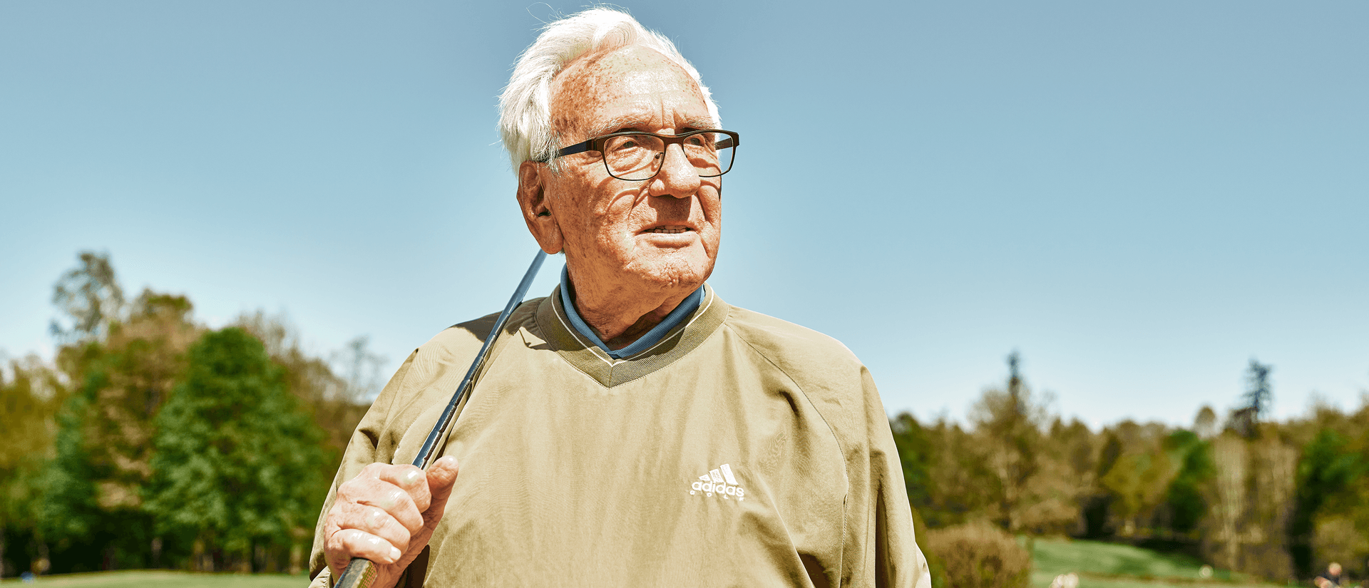 Älterer Mann mit Golfschläger auf dem Golfplatz, umgeben von grüner Landschaft