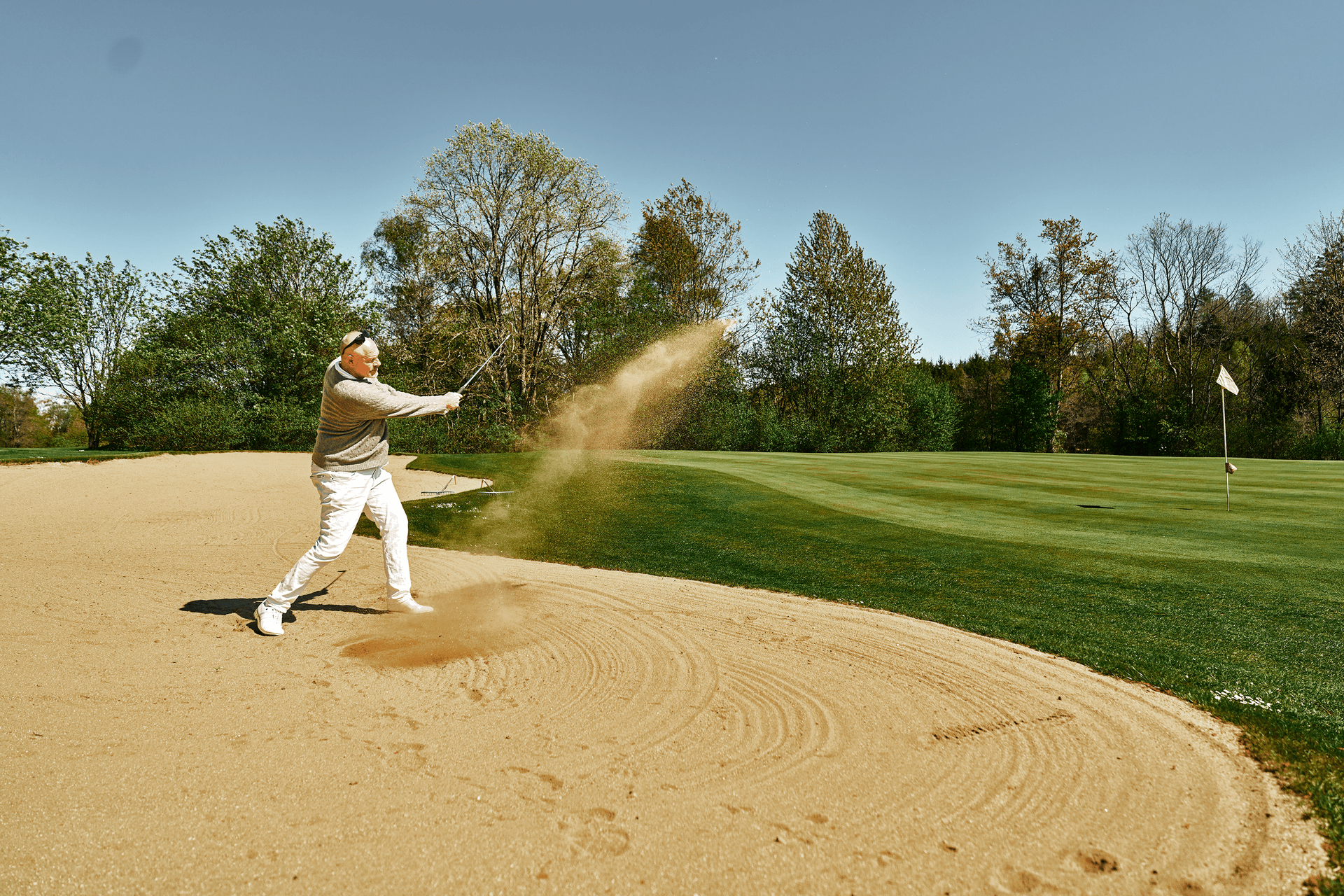 Golfer schlägt aus dem Bunker Richtung Fahne auf grünem Fairway.