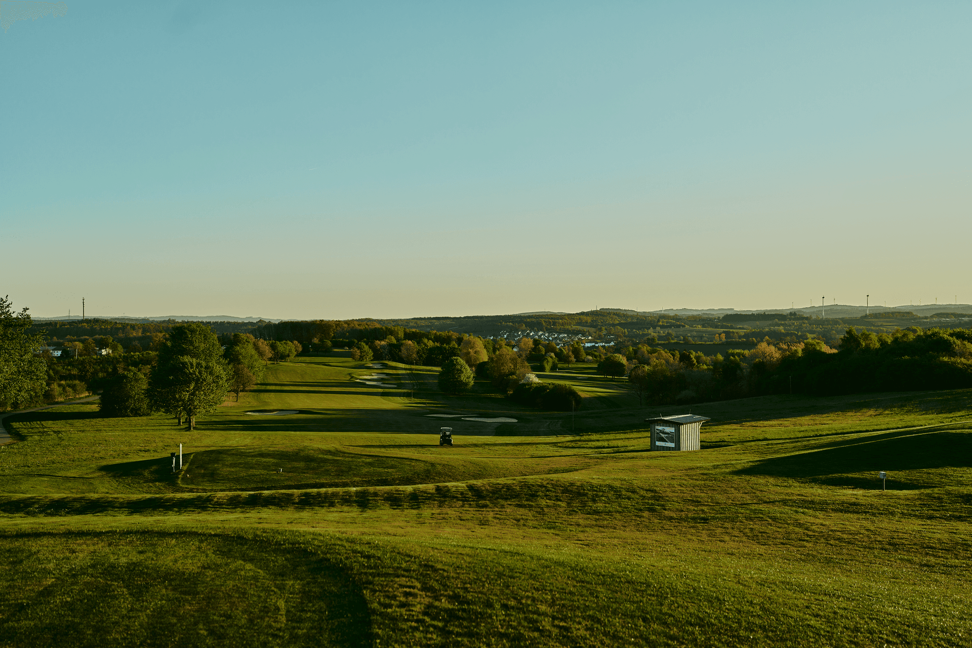 Weitläufige Golfplatzlandschaft im Abendlicht mit Blick auf sanfte Hügel.